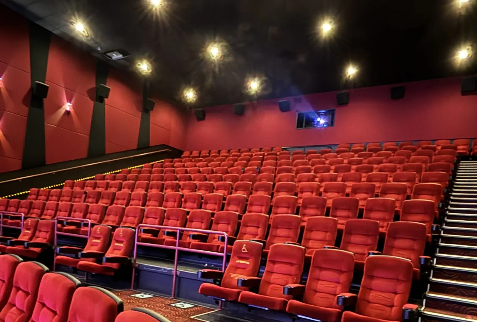 Salle de cinéma vide aux fauteuils rouges, cabine de projection au fond.